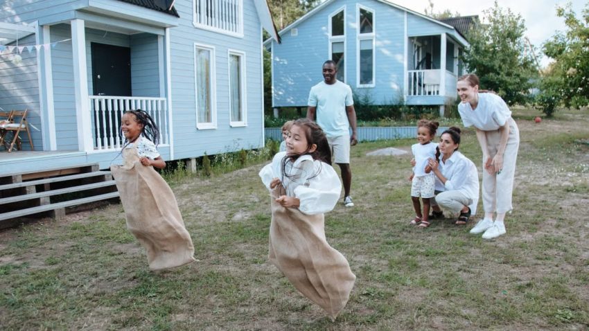 Group of children enjoying a sack race in a backyard setting, surrounded by family.